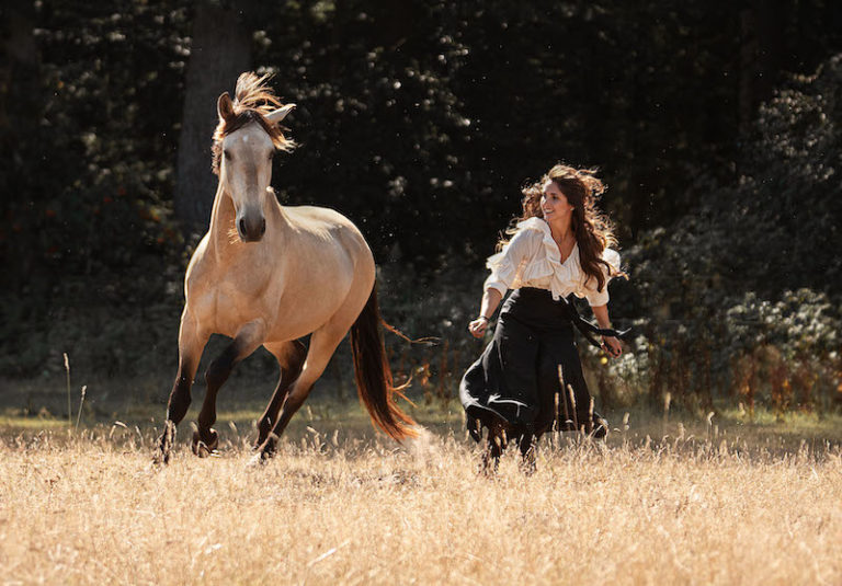Rider runs across meadow in summer with her Lusitano at Picadera