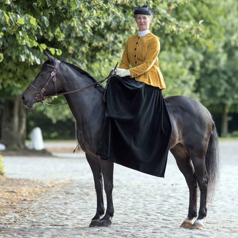 Dame mit Reitrock im Damensattel auf schwarzem Pferd bei Picadera